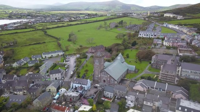 4k Aerial Drone Shot of Dingle, Ireland During the Rain Season. Lush Green Farms and Landscapes Nearby. Small Town Church in Focus of Shot. Colorful Houses and Tiny Roads Weaving Through Green Grass