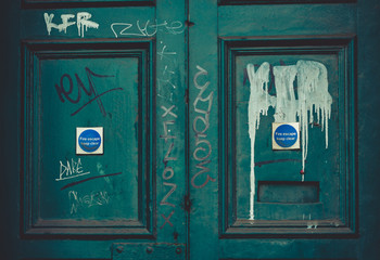 A light blue abandoned fire door with graffiti painted over it.