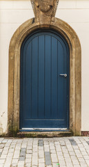 An old blue door on a white wall with a silver handle, probably from a  church