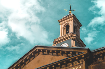A weather vane on top of a clock tower of an old building against a bright blue sky.