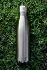 Stainless thermos water bottle isolated on green grass outdoor. Steel color. Vertical photo without effects.