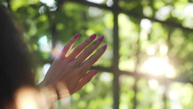 Sun flares through hand and fence in slow motion, hiding from the sun, pink finger nails, closing eyes, white flare, flash, hot summer rays