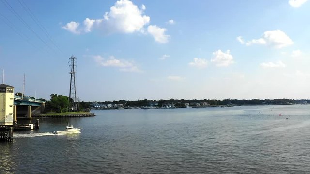 Aerial drone shot over a large river leading out to the ocean with a white boat under blue skies in Brielle, New Jersey.