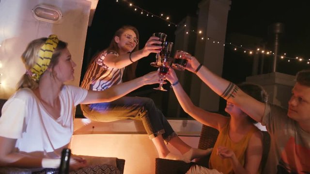 Group of young stylish Caucasian people holding drinks in hands, clinking glasses. Friends spending amazing time together in evening. Weekend. Cheers. Lifestyle.
