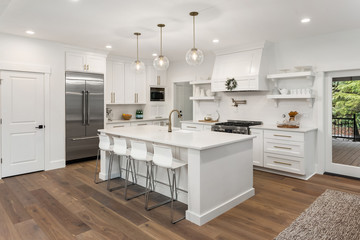 beautiful kitchen in new luxury home with island, pendant lights, hardwood floors, and stainless steel appliances