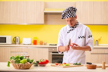 Young professional cook preparing salad at kitchen