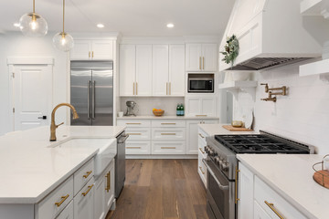Beautiful kitchen detail in new luxury home. Features island, pendant lights, hardwood floors, and stainless steel appliances - obrazy, fototapety, plakaty