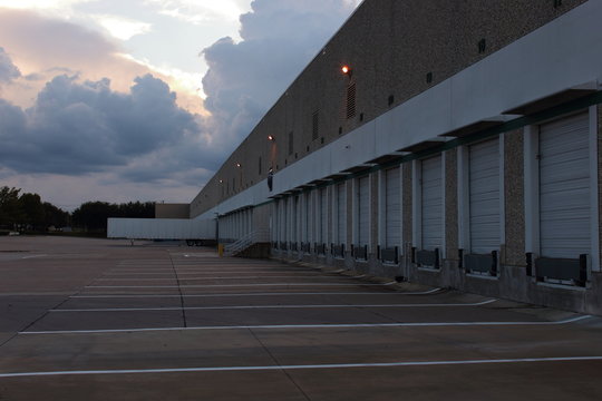 A Empty Loading Dock At Sunset, Soon It Will Be Filled With Trucks And Trailers Delivering The Freight From Around The World.lights Just Coming On And There's Clouds In The Background 