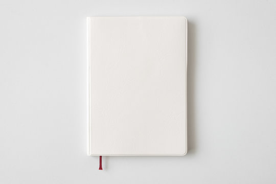 Top view of closed blank white leather cover notebook on white desk background with copy space