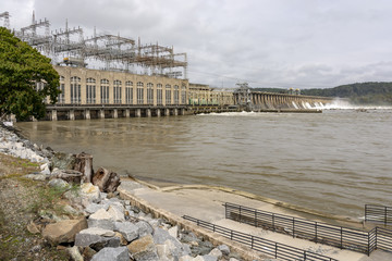 An industrial looking dam, made of concrete and steel, crosses a brown and muddy looking...
