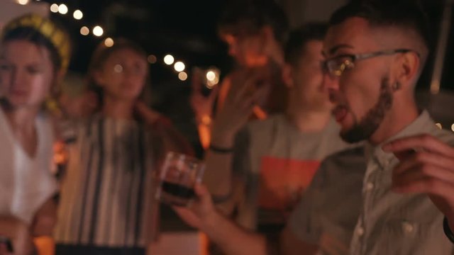 Five best friends holding dancing together at party. Likable Caucasian hipsters holding glasses in hands, having fun. Outdoors. Evening. Summertime.