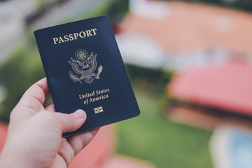 Human hand holding an American passport in front of a blurry background USA travel