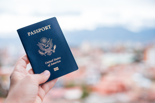 One single hand holding a blue American passport in front of a blurry background