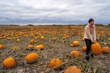 Adult woman (30s) attempts to pick up a giant pumpkin from a pumpkin patch. Smiling and laughing...