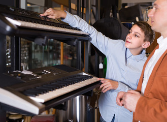 Father and teenage son examining keyboards in guitar shop