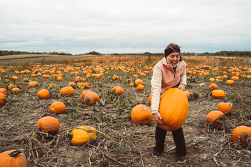 Adult woman (30s) attempts and struggles to lift and to pick up a giant pumpkin from a pumpkin patch. Smiling and laughing and having fun