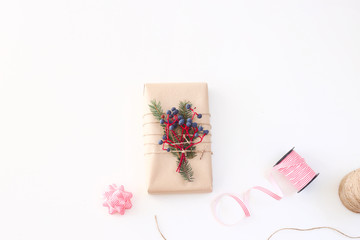 Christmas New Year's gift decorated with craft paper and berries on a white background next to the ribbon and bow. Top view, flat lay