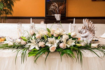 a bouquet of white lilies and roses, palm leaves, candles, an angel statue, glasses of the newlyweds on the festive table - decoration