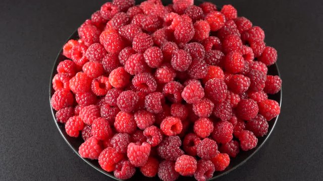 Fresh, ripe, juicy raspberry background, close up berry, rotation loopable 4k . Food  background. Gastronomy concept, organic food. Macro red raspberries fruit in plate on black background