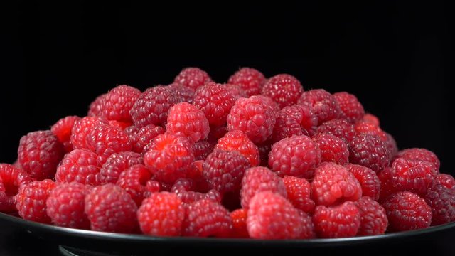 Fresh, ripe, juicy raspberry background, close up berry, rotation loopable 4k . Food  background. Gastronomy concept, organic food. Macro red raspberries fruit in plate on black background
