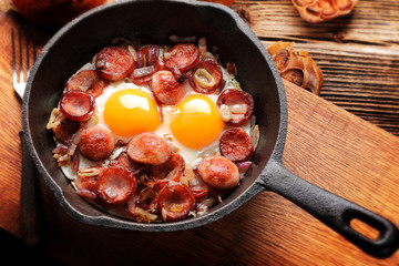 Cooked egg and sausages on rying pan, tasty english breakfast on wooden background