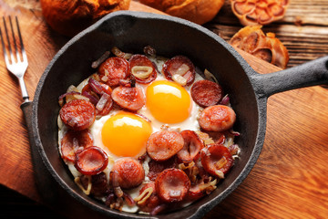 Cooked egg and sausages on rying pan, tasty english breakfast on wooden background