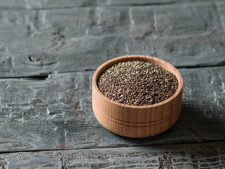 Wooden bowl with black Chia seeds on dark table.