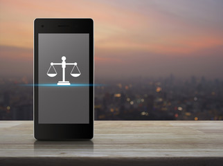 Law flat icon on modern smart mobile phone screen on wooden table over blur of cityscape on warm...