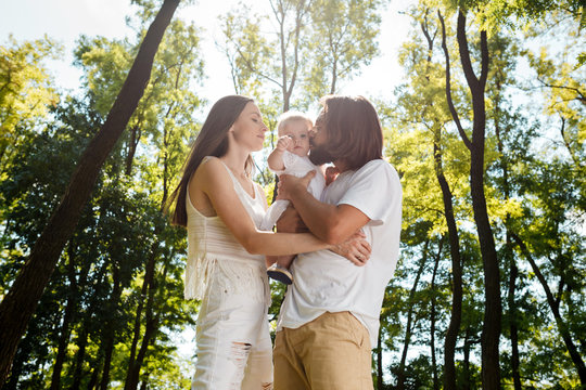 Happy family on the open air. Young dark-haired woman and her husband are kissing their charming little daughter.