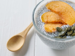 Peach slices with Chia pudding and pumpkin seeds on a white wooden table.