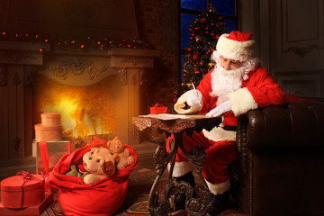 Portrait of happy Santa Claus sitting at his room at home near Christmas tree and answering Christmas letters. © ty