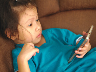 Little Asian kid using smartphone on sofa bed.