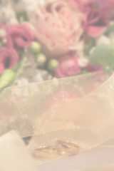 Fototapeta premium Wedding blurred background: wedding rings near the natural roses bouquet vertical