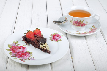 Piece of delicious homemade brownie cake with strawberries and tea  on white table. Selective focus