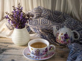 Home interior decor, bouquet of mauve flowers in a vase and blue fabric on rustic wooden table, with a white curtain background