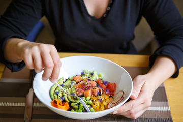 Woman eats poke bowl with salmon, avocado and vegetables for lunch