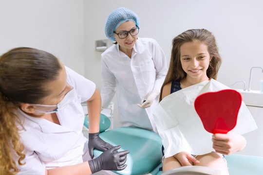 Happy child patient looking in the mirror at the teeth, sitting in the dental chair
