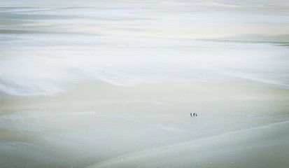 vision of a group of tourists walking on the sand, in the mudflat, around the famous Mont Saint Michel Abbey, at low tide.
