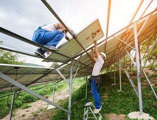 Solar photo voltaic panel system installing. Two technicians standing on ladder and platform top mounting heavy solar panel. Investment in alternative energy and professional construction concept. © anatoliy_gleb