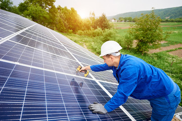 Construction worker connects photo voltaic panel to solar system using screwdriver. Professional installing and construction of solar system, alternative energy and financial investment concept.