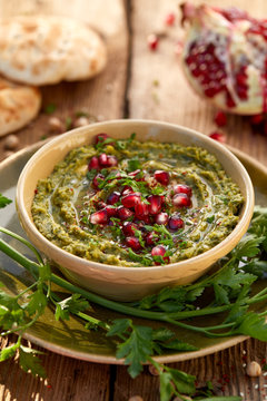 Hummus. Herbal hummus with the addition of pomegranate seeds, parsley, olive oil and aromatic spices in a ceramic pot on a wooden rustic table. A healthy and delicious vegan spread, dip 