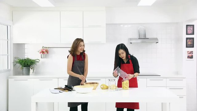 Time lapse video, beautiful Asian woman in red shirt and black  apron teaching her daughter how to arrange things for decoration and cooking in white clean modern kitchen