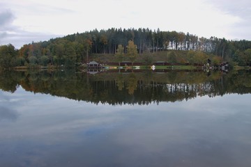 Obraz premium Lake Hollerersee, a small moorland lake in Upper Austria, in autumn. Forest and buildings reflect in the dark water. Haigermoos, Austria, Europe. 
