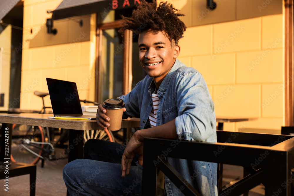 Sticker Happy young african man sitting at the cafe outdoors