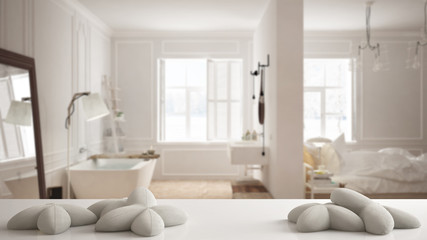 Obraz na płótnie Canvas White table, desk or shelf with five soft white pillows in the shape of stars or flowers, over blurred scandinavian bedroom with bathroom, minimal architecture interior design concept