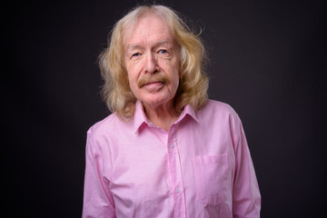 Senior businessman wearing pink shirt against gray background