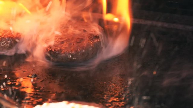 Delicious beef burgers are frying on the hot iron with flames and smoke in UHD