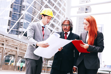 Three people with different professions in urban city outdoor scene - one engineer with blueprint and other two business people.