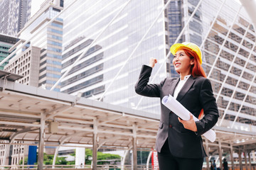 Successful and smiling happy female business woman in hard helmet and blueprint in urban city outdoor scene - engineering and architecture people concept.