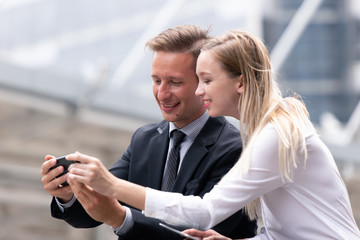 couple business people looking at smartphone together and smile outdoor office building background.